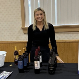 Hannah Curty poses behind a wine tasting booth