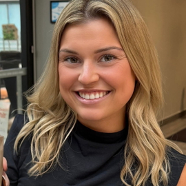A close‑up of Hannah Curty smiling inside a cafe and holding a beverage